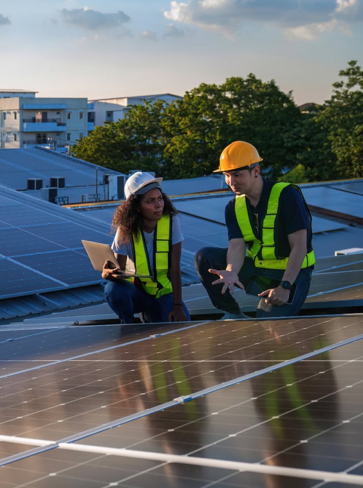 A man and a woman who are electrical engineers are sitting on a roof discussing the set up of a recent commercial solar panel installation.